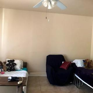 A cozy living room with a sofa, chair, and table adorned with pillows and teddy bears, under a ceiling fan.