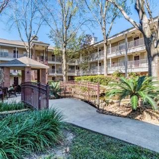 An exterior view of a multi-story apartment building with well-maintained landscaping and a central pathway.