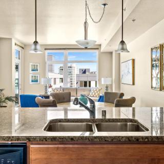 A modern open floor plan featuring a kitchen with a double sink and countertop overlooking a bright living room with large windows.