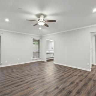 A spacious, empty living room with hardwood floors and a ceiling fan.