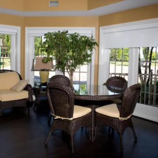 A cozy living room with wicker furniture, a glass table, and an indoor plant, bathed in natural sunlight.