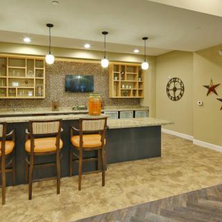 A modern home bar featuring a kitchen island with bar stools, pendant lighting, and stylish shelving.