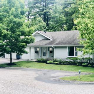 A suburban house surrounded by trees and greenery, with a driveway leading to the entrance.