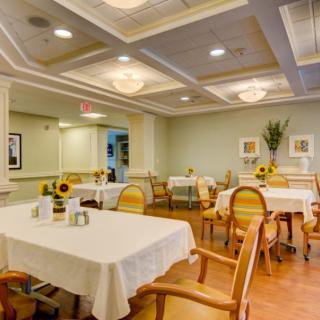 A well-lit dining room with neatly arranged tables and chairs, decorated with sunflowers and art pieces on the walls.