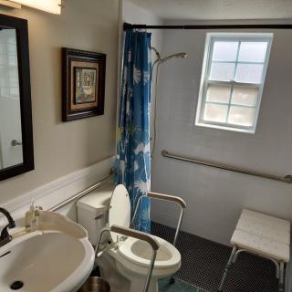 An accessible bathroom with grab bars, a shower bench, and a blue shower curtain.