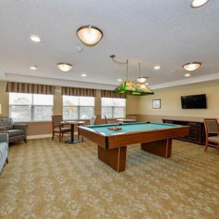A spacious and well-lit game room featuring a pool table, seating areas, and a wall-mounted television.