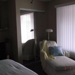 A cozy living room corner with a chaise lounge and reading lamp, complemented by window blinds and a mirror.