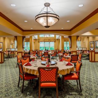 An elegant dining room with neatly arranged tables and chairs, featuring a large chandelier overhead.