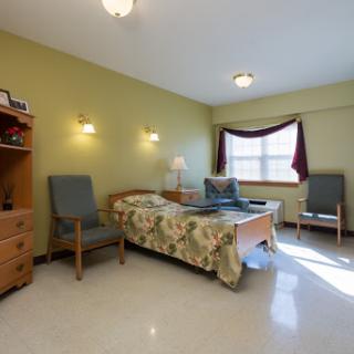 A cozy and well-lit bedroom featuring a single bed, two chairs, and a dresser.
