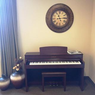 A digital piano with a bench sits beneath a decorative wall clock in a cozy room.