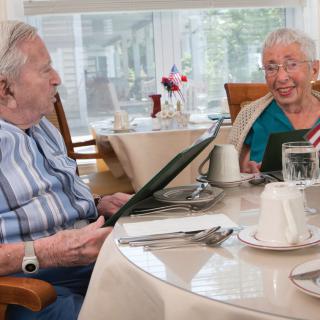 Two elderly individuals enjoying a conversation while looking at menus in a dining setting.