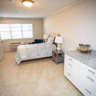 A cozy bedroom with a neatly made bed, bedside tables with lamps, and a dresser under a large window.