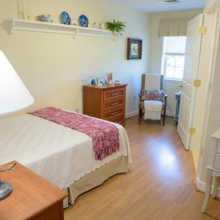 A cozy bedroom with light-colored walls, a bed, and a window letting in natural light.