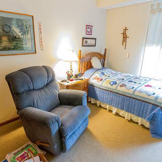 A cozy bedroom with a recliner chair and a single bed adorned with a colorful quilt.