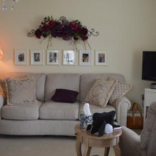 A cozy living room with a comfortable sofa, adorned with cushions, decorative flower arrangement and framed pictures on the wall.