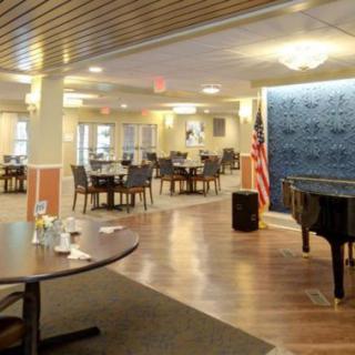 A spacious dining area with tables and chairs, featuring a grand piano and wooden flooring.