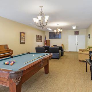 A cozy game room featuring a pool table, sofas, a piano, and a television.