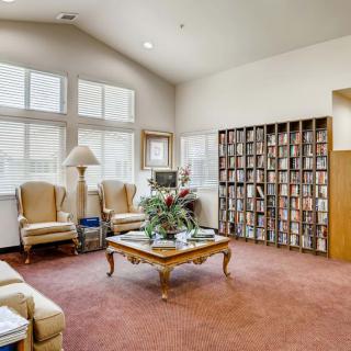 A cozy library room with a large bookshelf, comfortable chairs, and natural light coming through the windows.