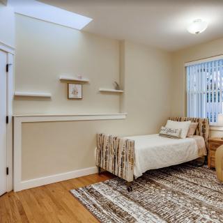 A minimalist bedroom with a single bed, shelves, and a window, featuring neutral colors and a wooden floor.
