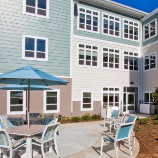 A residential building with an outdoor patio area featuring tables, chairs, and a large umbrella.