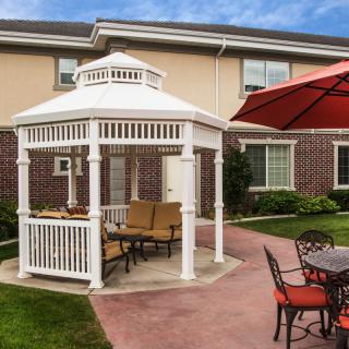 A cozy outdoor patio featuring a white gazebo with seating and a large red umbrella nearby.