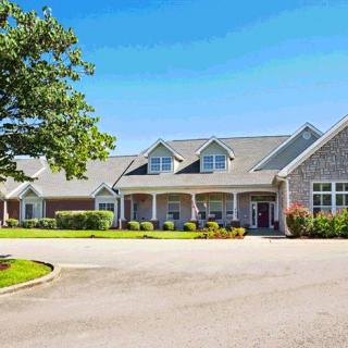 A large residential-style building with a neatly paved driveway and surrounding greenery against a clear blue sky.