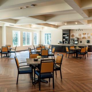 A spacious, well-lit dining area with wooden floors and multiple tables and chairs.