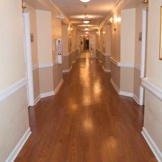 A well-lit, empty hallway with wooden floors and beige walls.