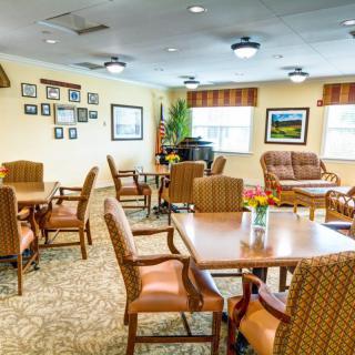 A well-furnished dining and lounge area with tables, chairs, and a piano, offering a cozy setting.