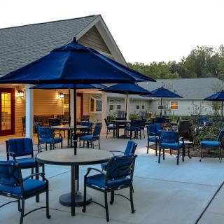 An inviting patio area with tables, chairs, and blue umbrellas is set up outside a building during the early evening.