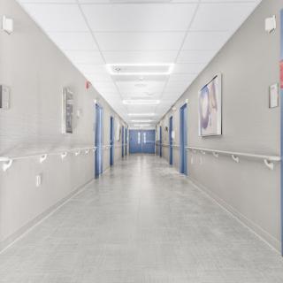 A spacious and well-lit corridor in a hospital, featuring blue doors and minimalist design.