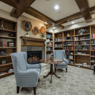 A cozy library room with bookshelves, a fireplace, and comfortable seating.