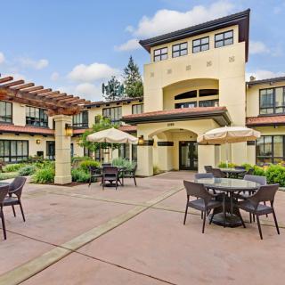A courtyard with outdoor seating and umbrellas in front of a large building on a sunny day.