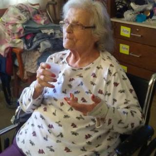 An elderly woman sitting in a wheelchair, enjoying a moment with a cup in her hand.