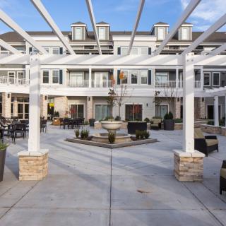 A bright and open courtyard with a pergola and outdoor seating, set against a multi-story residential building facade.