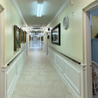 A well-lit hallway with paintings and a clock on the walls.
