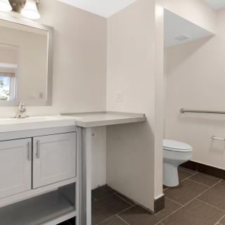 A modern bathroom with a sink, mirror, and toilet, featuring a countertop space and tiled flooring.