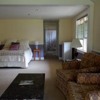 A comfortable bedroom with a bed, seating area, and natural light.