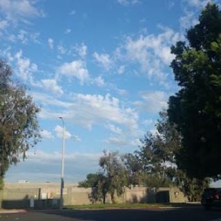 A serene landscape featuring a clear blue sky with scattered clouds and lush greenery.