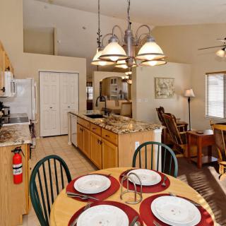 A modern open floor plan kitchen and dining area featuring a granite countertop, wooden dining table with place settings, and stylish lighting fixtures.