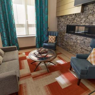 A cozy living room featuring a modern stone fireplace, blue armchairs, and a vibrant orange rug.