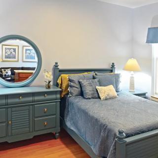 A cozy bedroom with blue-toned furniture, including a bed and dresser with a round mirror, complemented by a table lamp.