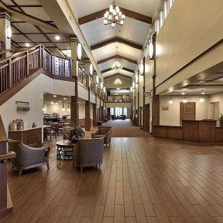 A spacious hotel lobby with elegant wood flooring, cozy seating areas, and a high ceiling adorned with chandeliers.