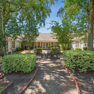 A serene garden setting with a patio and outdoor furniture, surrounded by lush greenery.
