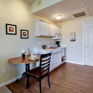 A cozy kitchen area with a small dining table and chair, featuring white cabinets and wooden flooring.