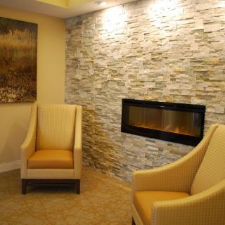 A modern living room featuring a stone wall with a built-in fireplace, paired with comfortable armchairs.