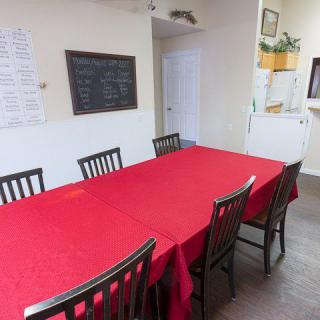 A dining area with a red tablecloth-covered table surrounded by chairs, featuring a chalkboard menu on the wall.