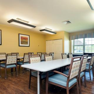 A well-lit dining area with multiple tables and chairs, featuring artwork on the walls and large windows.