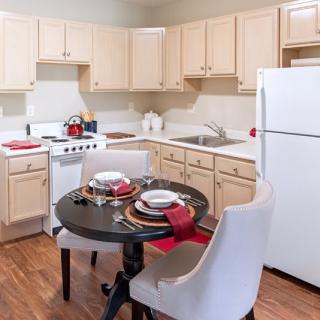 A cozy kitchen with a small dining area, featuring light-colored cabinets, a white refrigerator, and a set table for two.