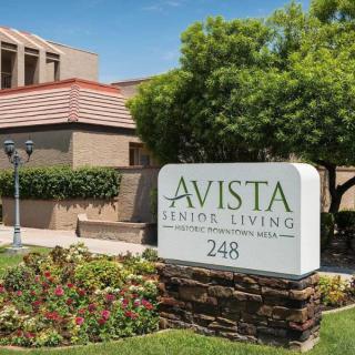 The image displays the entrance sign of Avista Senior Living, set against a backdrop of well-maintained landscaping and residential buildings.